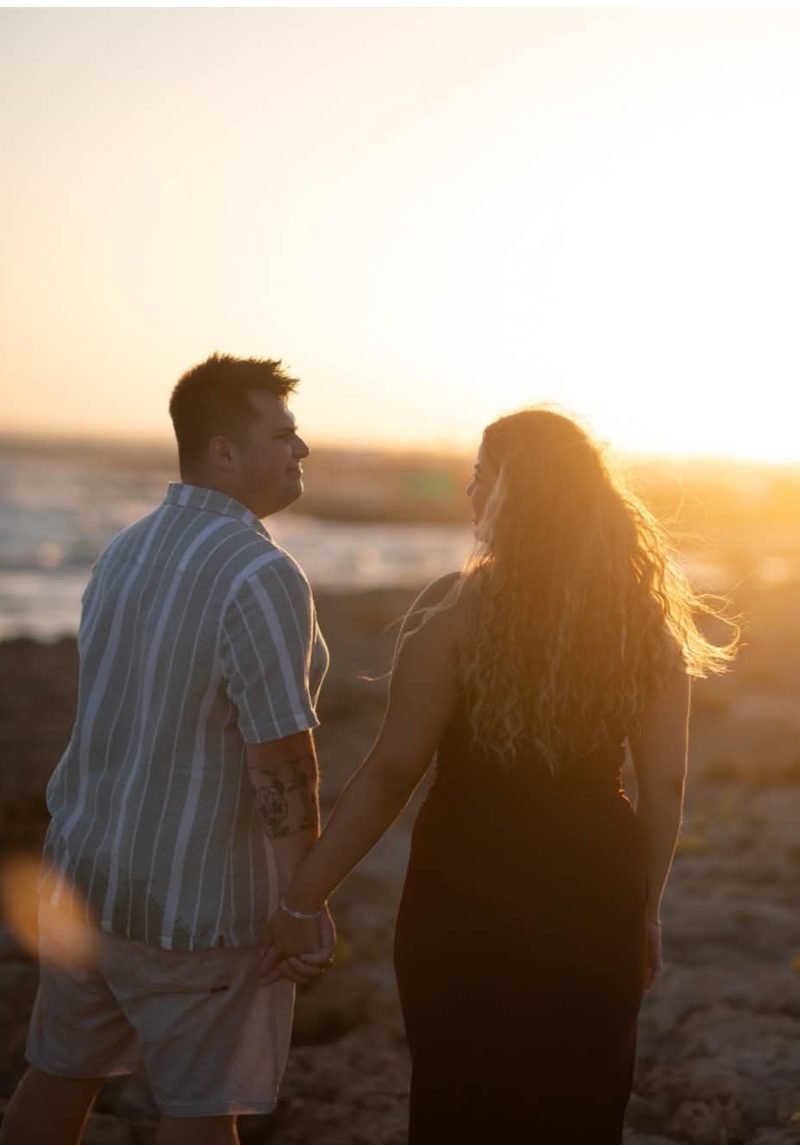 Liam and Andrea holding hands looking out to sea at sunset